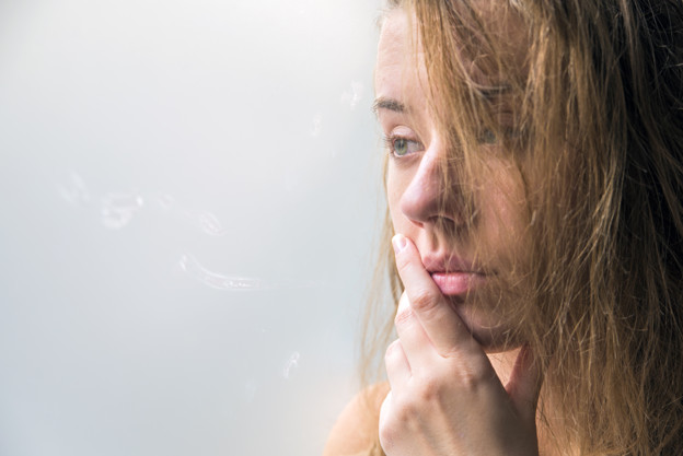 lonely girl near window thinking about something. beautiful sad lonely girl sitting near the window is missing